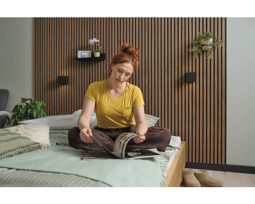 Chambre à coucher confortable avec des panneaux de bois au mur, une femme assise sur le lit et des éléments décoratifs tels que des plantes et des appliques murales.