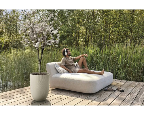 Szene im Freien mit blühendem Baum im Pflanzgefäß und Mann auf einer Liege mit Kissen