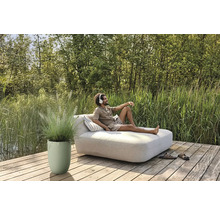 Mann entspannt mit Kopfhörern auf einer Gartenliege auf einer Holzterrasse neben einem Pflanzgefäß mit Ziergras.