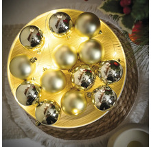 Dekorative goldfarbene Christbaumkugeln auf einem Teller mit Lichterkette