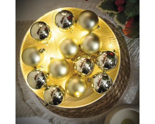 Dekorative goldfarbene Christbaumkugeln auf einem Teller mit Lichterkette