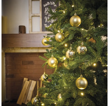 Dekorierter Weihnachtsbaum mit goldenen und silbernen Christbaumkugeln und Lichtern in einem Wohnzimmer mit Kamin