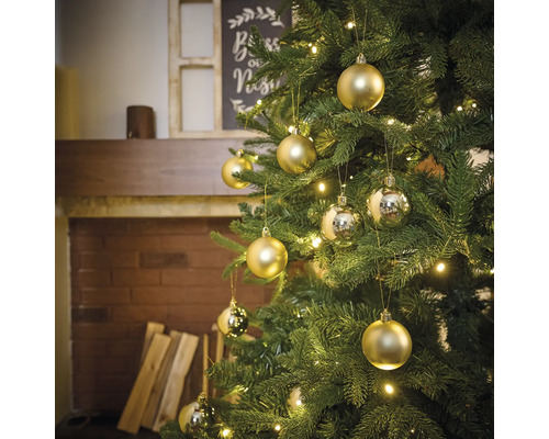 Dekorierter Weihnachtsbaum mit goldenen und silbernen Christbaumkugeln und Lichtern in einem Wohnzimmer mit Kamin