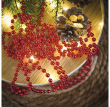 Décoration avec collier de perles rouges, branches de sapin, guirlande lumineuse et pommes de pin sur une assiette