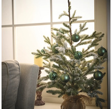 Sapin de Noël décoratif avec boules vertes et sac en jute sur une table devant une fenêtre.