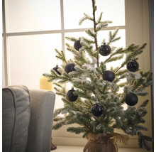 Dekorativer, schneebedeckter Weihnachtsbaum mit schwarzen Kugeln auf einem Tisch in der Nähe eines Fensters