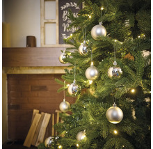 Sapin de Noël décoré avec boules et guirlande lumineuse devant la cheminée