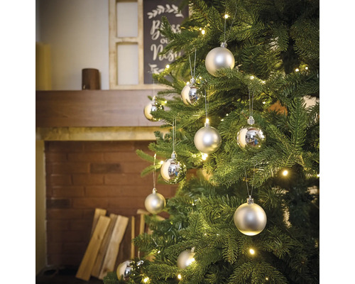Sapin de Noël décoré avec boules et guirlande lumineuse devant la cheminée