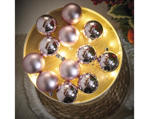 Boules de Noël décoratives roses sur un plateau en bois avec des lumières