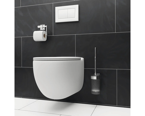 WC suspendu avec support de papier toilette, plaque de commande et brosse de toilette devant un fond de carreaux sombres.