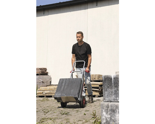 Un homme transporte des pavés avec un diable.