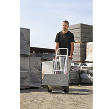 Mann transportéiert Trëttoirsteng mat enger Sakkar am Aussenberäich.