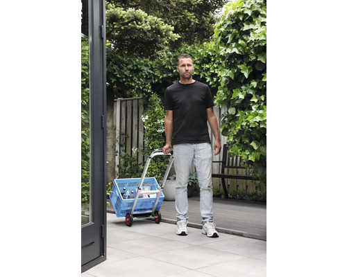 Mann transportiert blaue Einkaufsbox mit einem Trolley im Garten