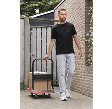Un homme tire un chariot de manutention avec des cartons sur un chemin pavé.