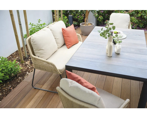 Scène de jardin avec canapé, coussins et table à manger sur une terrasse