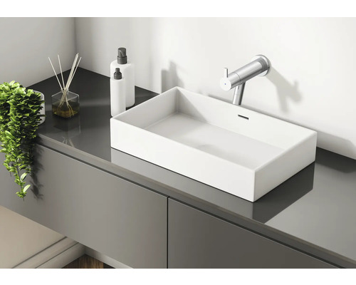 Modernes Badezimmer mit Waschbecken, Armatur, Duftstäbchen und Lotion-Spendern auf einem grauen Waschtisch.