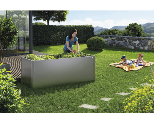 Jardin avec potager surélevé en métal, planté de légumes, pendant qu''une femme récolte et que des enfants jouent.