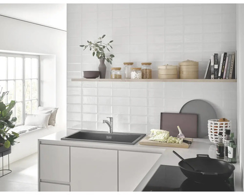 Helle Küche mit Spüle, Armatur, Wandfliesen und Küchenutensilien.