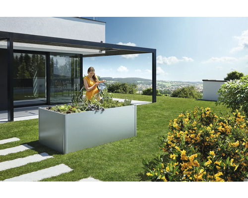 Frau gießt Pflanzen in einem Hochbeet im Garten