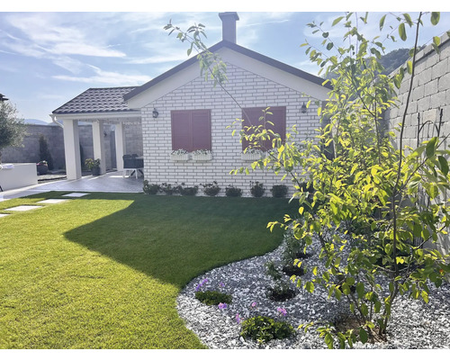 Ein Garten mit Rasenfläche, Kiesbeet und einem Haus mit roten Fensterläden.