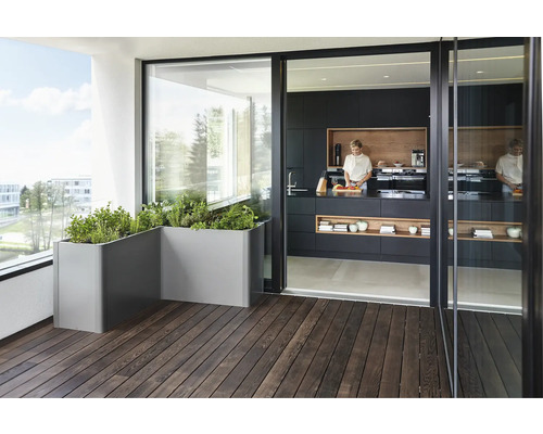 Balcon avec bacs à fleurs gris et vue sur une cuisine avec kitchenette noire