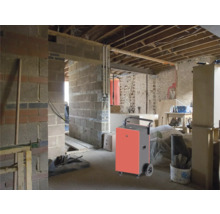 Déshumidificateur dans une pièce brute avec des murs en briques et des poutres de plafond apparentes.