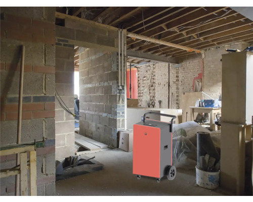 Déshumidificateur dans une pièce brute avec des murs en briques et des poutres de plafond apparentes.