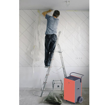 Un homme sur une échelle effectuant des travaux de rénovation avec un déshumidificateur de chantier dans la pièce.