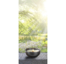 Bougie parfumée allumée dans un bol devant un étang de jardin flou