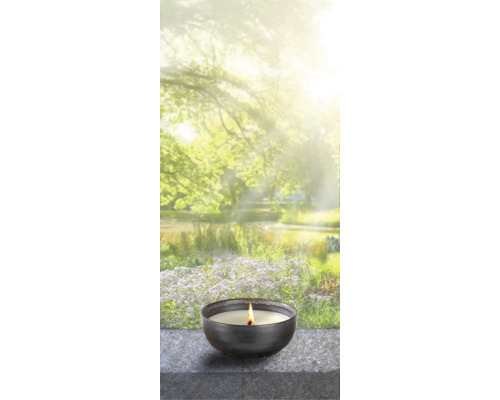 Bougie parfumée allumée dans un bol devant un étang de jardin flou