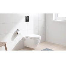 Hänge-WC mit Betätigungsplatte und Toilettenpapierhalter in einem Badezimmer mit weißen Fliesen.