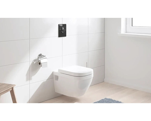 Hänge-WC mit Betätigungsplatte und Toilettenpapierhalter in einem Badezimmer mit weißen Fliesen.