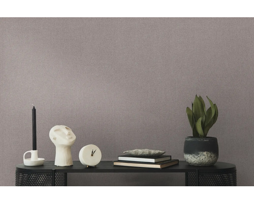 Nahaufnahme einer gemusterten Tapete mit Tisch, darauf Kerze, Skulptur, Uhr, Bücher und einer Topfpflanze.