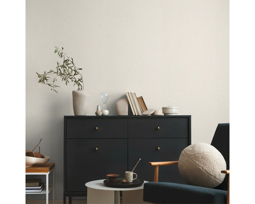 Salon avec commode, chaise et objets de décoration devant un papier peint clair à motifs