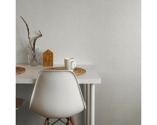 Scène avec une table, une chaise, une tasse, un vase et une décoration devant un papier peint mural.