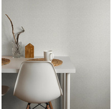 Scène avec du papier peint texturé au mur, une table, une chaise, un verre, une maison en bois et une tasse