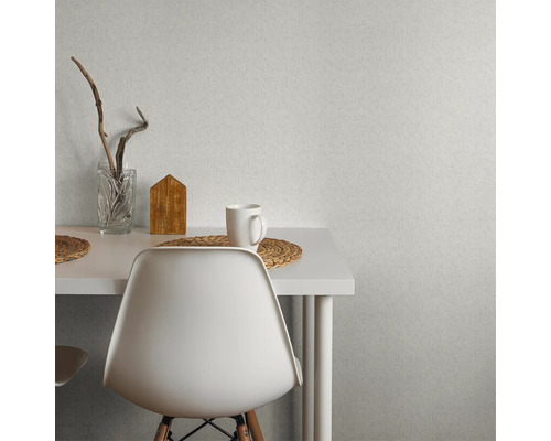 Scène avec du papier peint texturé au mur, une table, une chaise, un verre, une maison en bois et une tasse