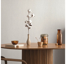 Décoration de table avec branche de coton, bol, livre, pot de conservation et bouteille sur une table en bois devant un mur uni.