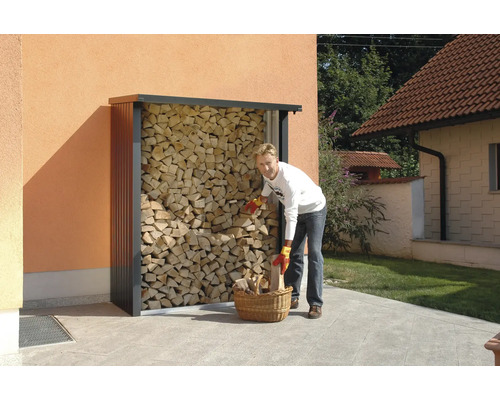 Une personne remplit un panier à bois près d''un range-bûches