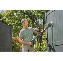 Un homme nettoie un portail avec une brosse électrique dans le jardin.