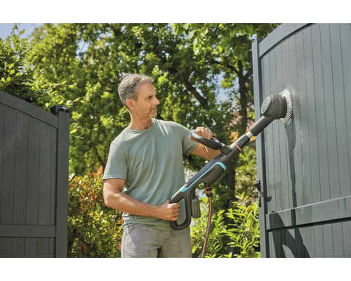 Un homme nettoie un portail avec une brosse électrique dans le jardin.