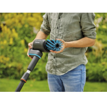 Une personne tient une brosse Gardena pour le nettoyage des surfaces extérieures