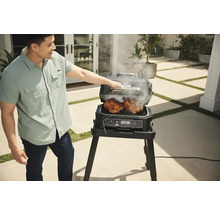 Mann grillt zwei Hähnchen mit einem elektrischen Ninja Grill im Freien.