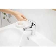 Une personne actionne un mitigeur de lavabo chromé sur un lavabo.