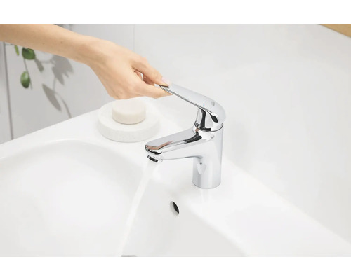 Une personne actionne un mitigeur de lavabo chromé sur un lavabo.