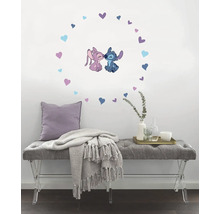 Wanddekoration mit Stitch und Angel, umgeben von Herzen, über einer grauen Sitzbank mit Kissen und Decke