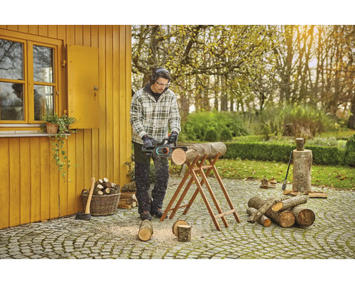 Un homme coupe du bois avec une tronçonneuse dans le jardin.