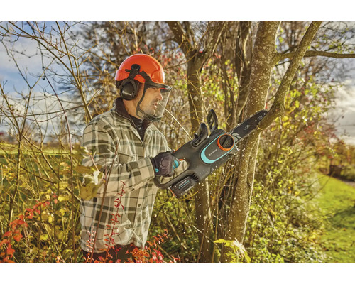 Homme avec casque de protection et tronçonneuse à batterie Gardena coupant un arbre.