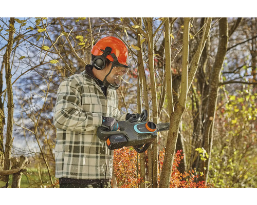 Homme avec casque de sécurité et tronçonneuse à batterie coupant un arbre