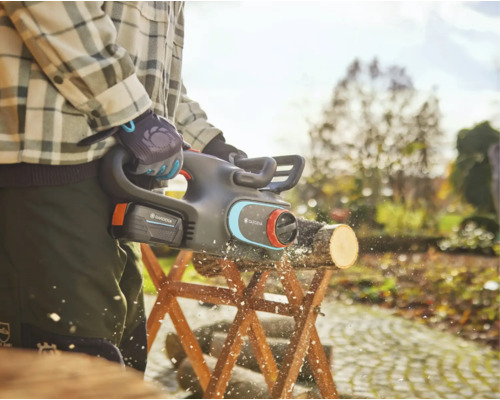 Jardinier sciant une bûche avec une tronçonneuse à batterie sur un chevalet dans le jardin.